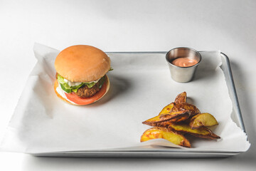 Bacon burger with beef patty, fresh tomatoes and cucumbers with sauce served on a metal tray over...