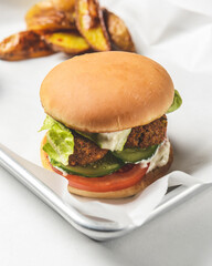 Bacon burger with beef patty, fresh tomatoes and cucumbers with sauce served on a metal tray over white background.
