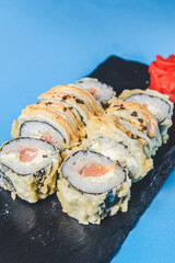 Japanese Sushi Roll - Warm Sushi Roll with Salmon and Cream Cheese served on a black board over bright blue background.