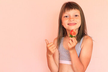 The concept of the benefits of early vitamin berries. Smiling eight-year-old girl holds a large strawberry, on a light background,in the other hand, the finger is raised up, close-up