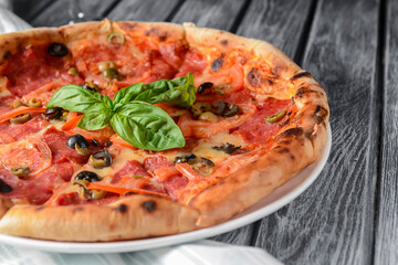 Fresh italian pizza with salami and black olives served over rustic wooden background. Traditional Italian pizza recipe