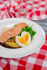 Salmon steak with fresh greenery and boiled eggs served on a white plate with a glass of wine.