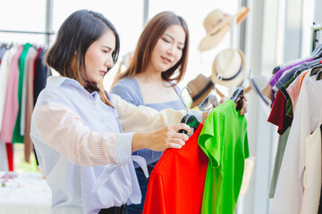 Naklejka na ściany i meble Women customer choosing clothes looking for new shirt in fashion shop with friend happy smile.