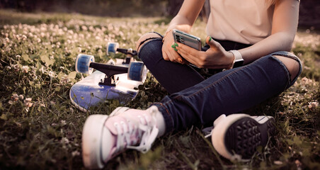 Girl skateboarder sitting on a board and using a smartphone, close-up