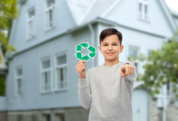 eco living, environment and sustainability concept - smiling boy holding green recycling sign and pointing to camera over house background