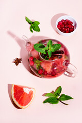 Immunity boosting drink. Mint Tea with cranberries, grapefruit and spices in glass teapot on pink table, trendy shadows