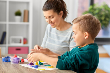 Obraz na płótnie Canvas family, creativity and craft concept - mother and little son playing with modeling clay at home