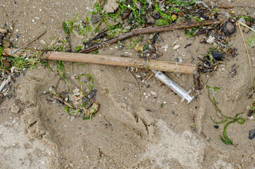A plastic syringe on the wet sand among the debris.