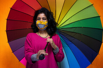 Beautiful young indian woman posing with a colored umbrella with covid 19 mask protection - Pretty...
