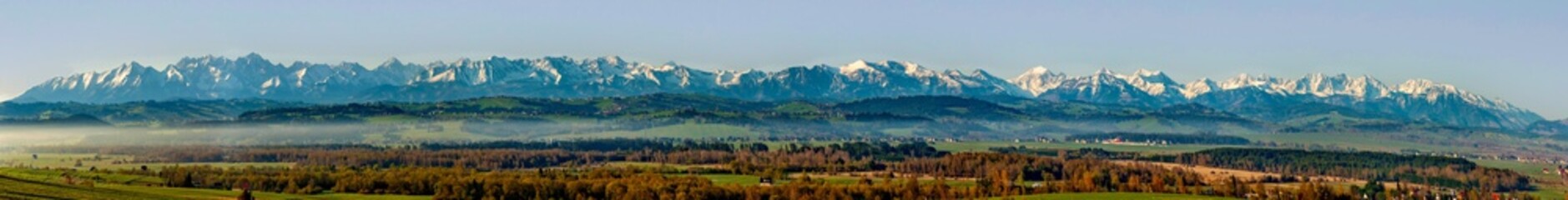 Extra wide panorama of the Tatra Mountains with forests, hills and meadows in Podhale region in Poland. Early morning in spring, morning fog, sunrise light