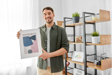 home improvement, decoration and people concept - happy smiling man decorating room with abstract picture in frame - Powered by Adobe