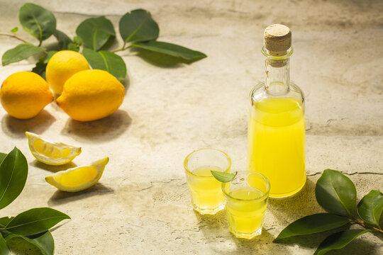 Summer table, limoncello in small glasses and bottle  - italian lemon liqueur, lemons. Hard light, stone background, copy space.