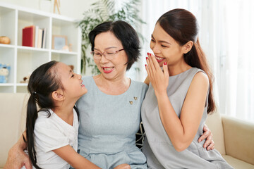 Mother and grandmother laughing at funny joke of preteen little girl, the are hugging and sitting...