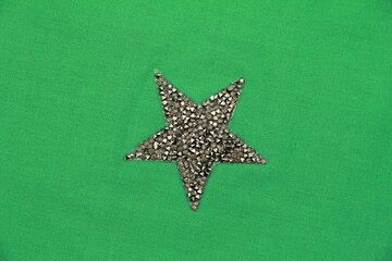 On the natural green linen fabric, an application in the form of a shiny star is applied.Creative hobbies, clothing recycling, masking holes in clothing, clothing design, tailoring with applique.