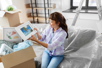 moving, people and real estate concept - happy smiling asian woman unpacking boxes at new home