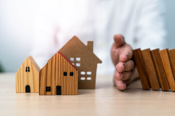 A male insurance agent defends his home from a falling domino. home insurance or home insurance