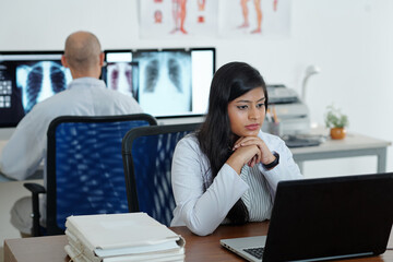 Obraz premium Pensive young female general practitioner working on computer and decoding medical tests of patient