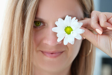 Obraz na płótnie Canvas Portrait of beautiful young woman with green eyes closes one eye with flower