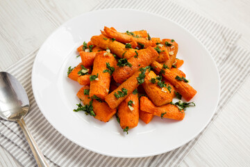 Homemade Roasted Carrots with Herbs on a white plate on a white wooden table, side view.