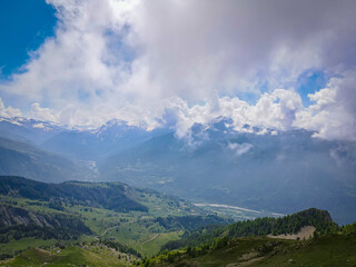 Vibrant aerial panoramic of the Alps during springtime. Snow capped peaks, forest covered valley and glacier fed streams and waterfalls