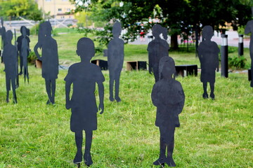 black figures of missing children made of plywood on a green lawn as an installation from a search...