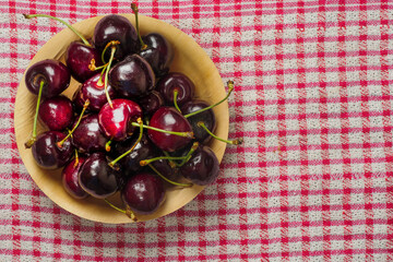 Red fresh juice cherry in a wooden bowl on a red and white table cloth. Close up. Fresh berries. Food industry. Produce product