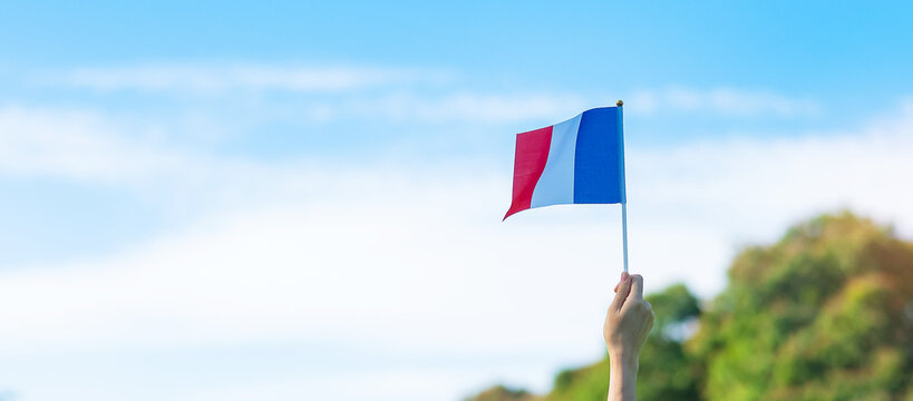 hand holding France flag on blue sky background. holiday of French National Day, Bastille Day and happy celebration concepts