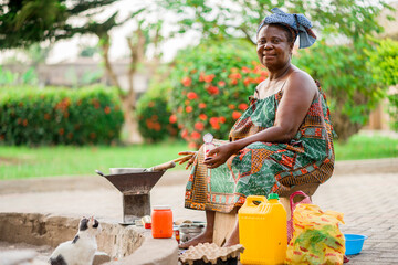 image of beautiful african mother sitting outside cooking- cheerful black woman preparing food with containers and plastics around her