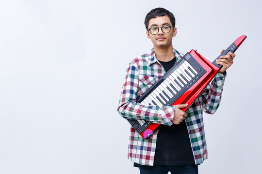 Portrait shot of handsome young teenage musician playing the keytar while looking at the camera in the studio. Young junior musician standing and holding keytar isolated with white background