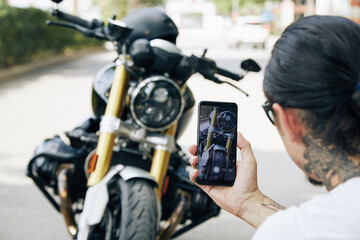 Fototapeta na wymiar Man taking cool photos of his motorcycle on smartphone to share with friends or post on social media