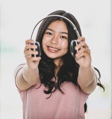 Portrait shot of attractive smiling young girl teenager listening to music with a headset and offer it to camera