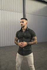 Hot caucasian man with arm tattoos in an emerald green shirt and white pants posing in the street