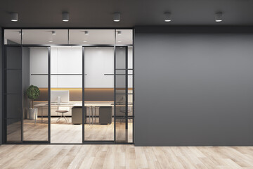 Black wall with copyspace for your text or logo next to doors to sunny office with monochrome style interior design, modern laptops on white tables and wooden floor. 3D rendering, mockup