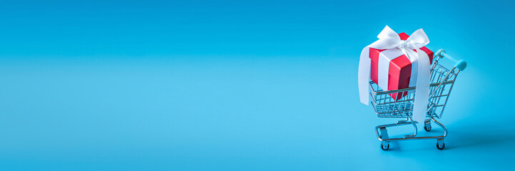 Gift box in a miniature supermarket trolley on a light blue background.