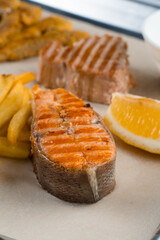 Fototapeta na wymiar Grilled salmon steak with lemon and fries on light background.