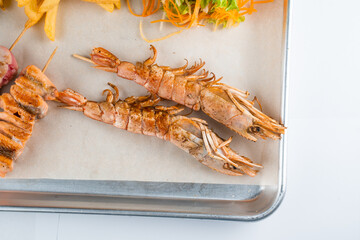Set of seafood with large grilled shrimps on metal plate with carrot, lettuce close-up.