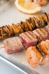 Barbecue seafood kebab with grilled mussels, tuna, salmon on a wooden skewer with white sauce and lemon.