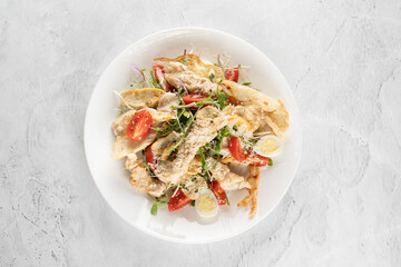 Caesar salad with chicken, parmesan, cherry tomato, lettuce, croutons, egg on white plate on light table