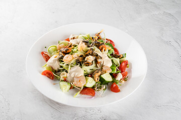 Salad with mussel, shrimp, tomato cherry, cucumber, zucchini pasta, microgreen, yogurt sauce on white plate on light table.