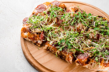 Pinsa romana with salami, cheese, mushrooms, decorated with microgreens on wooden boardon white background.