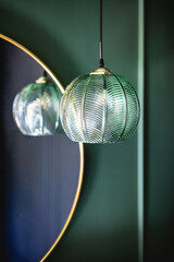 Elegant retro lamp hanging next to a mirror on dark green wall.