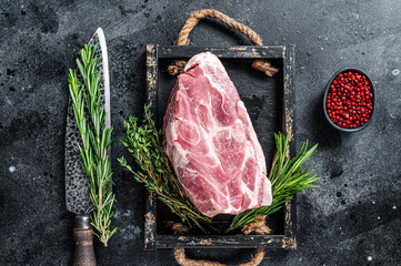 Raw pork neck meat piece for Chop steak in wooden tray with herbs. Black background. Top view