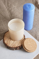 blue and beige aroma candle in a glass on a wooden podium from a saw cut from a tree. natural candles for aroma therapy