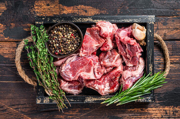 Raw lamb or goat meat diced for stew with bone. Dark wooden background. Top view