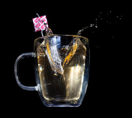 A tea bag with label fall into a glass mug with hot water,  on a black background