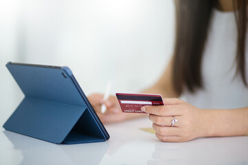 Focus on hand. young asian woman holding mock up of credit card and using digital tablet shopping or paying online