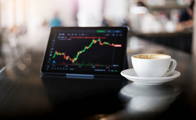 Soft focus of white coffee cup and blur digital tablet with cryptocurrency graph on screen