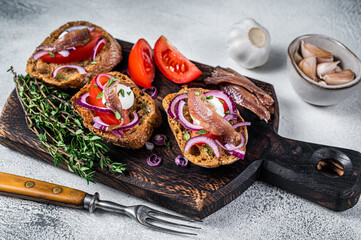 Toasts with olive oil, herbs, tomatoes and spicy anchovy fillets. White background. Top view