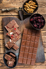 Dark chocolate bar with hazelnuts, peanuts, cranberries and freeze dried raspberries on a wooden board. wooden background. Top view