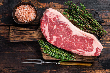 Raw new york strip beef steak or striploin on a wooden board. Dark wooden background. Top view